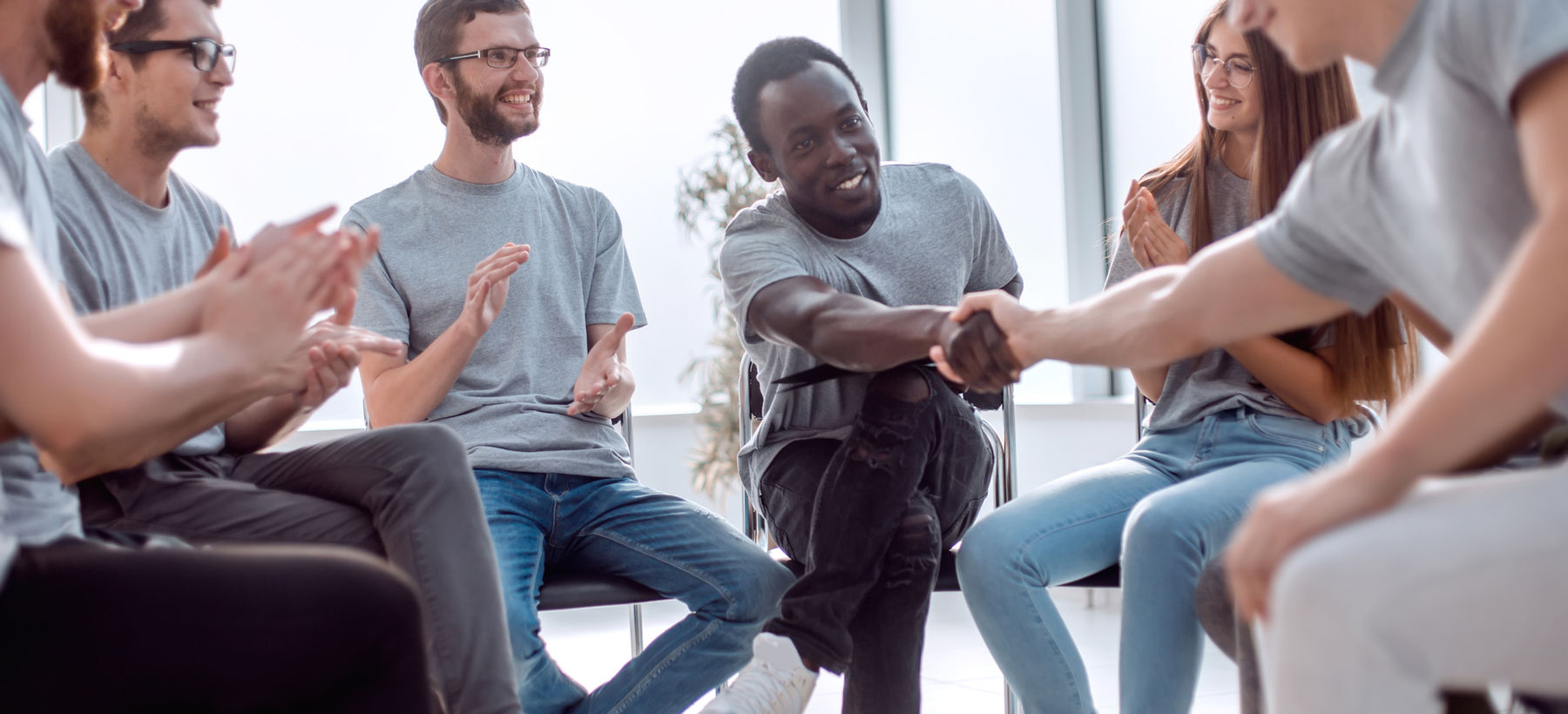 A small group sitting in a circle, two people shaking hands while the others clap